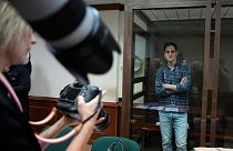 Il giornalista del Wall Street Journal Evan Gershkovich si trova in una gabbia di vetro mentre i fotografi lo immortalano in un'aula del tribunale di Mosca nell'aprile 2023.