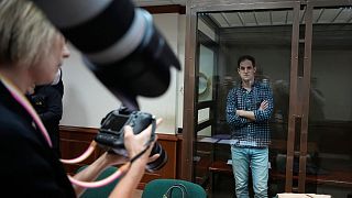 Le journaliste du Wall Street Journal Evan Gershkovich se tient dans une cage de verre tandis que des photographes le photographient dans une salle d'audience du tribunal de la ville de Moscou en avril 2023.