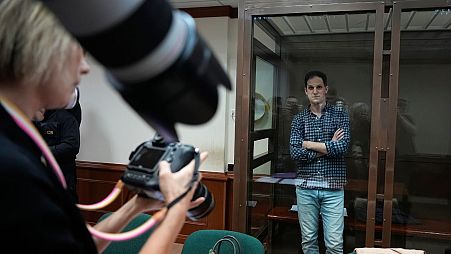 Wall Street Journal reporter Evan Gershkovich stands in a glass cage as photographers photograph him in a courtroom at the Moscow City Court in April 2023.