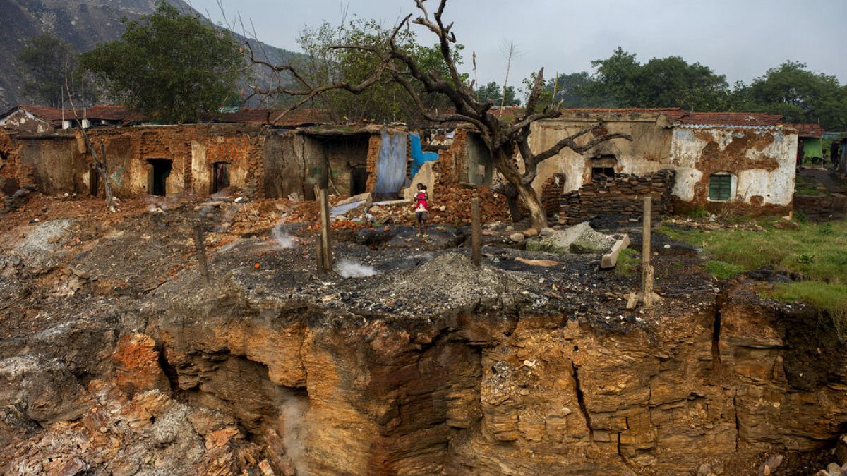 يتصاعد الدخان من شقوق الأرض بينما يحمل قروي طفله أمام المنازل المتضررة بسبب الانهيار بالقرب من دانباد