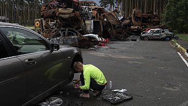 Un hombre repara su coche mientras varios vehículos destruidos por los ataques rusos se amontonan en un solar en Irpin, Ucrania, el viernes 7 de julio de 2023.