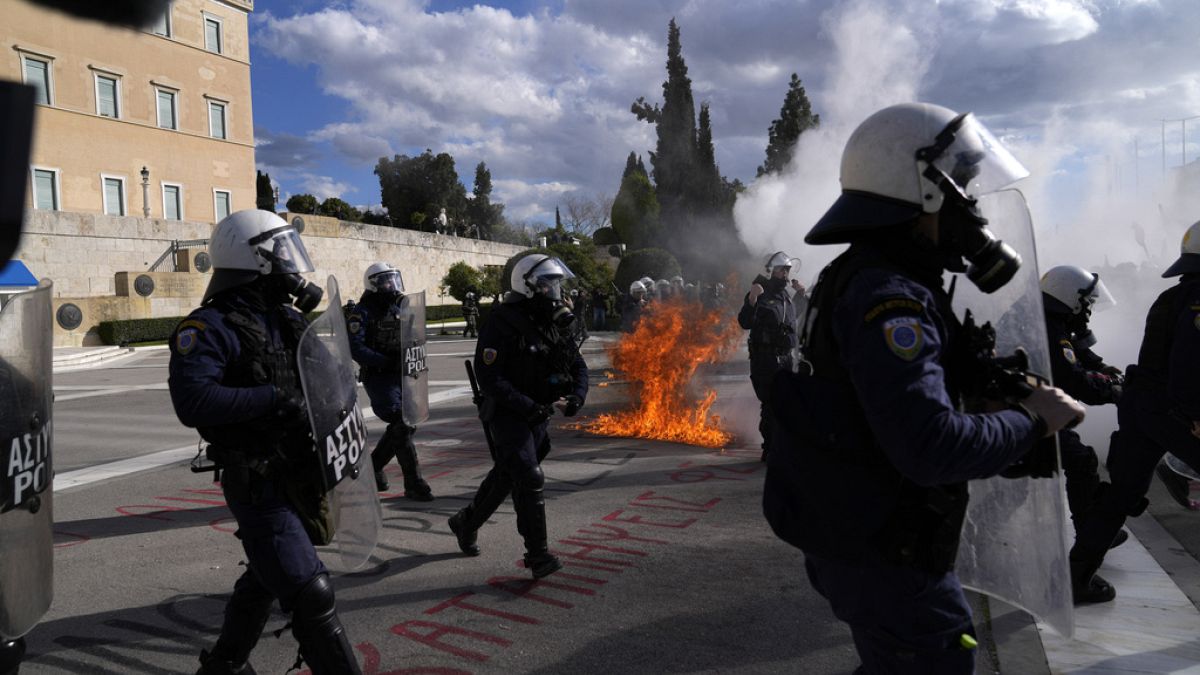 La polizia antisommossa si trova davanti al Parlamento mentre sullo sfondo si vede il fuoco di una molotov durante una manifestazione di studenti ad Atene, in Grecia, l'8 marzo 2024.