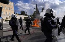 Unruhestifter stehen vor dem Parlament, während im Hintergrund das Feuer eines Molotowcocktails während einer Studentendemonstration in Athen, Griechenland, zu sehen ist, 8. März 2024
