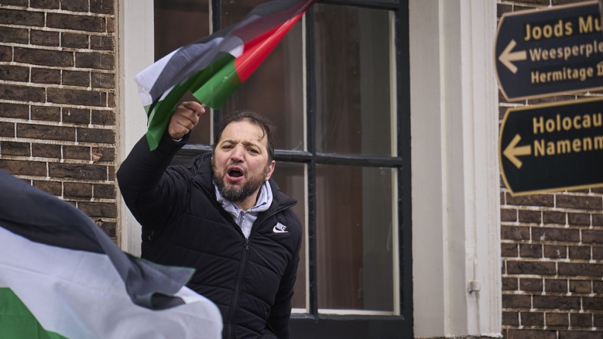 A man waves a Palestinian flag next to signs for the Holocaust Monument and the Jewish Museum as demonstrators protested against Israel's President Isaac Herzog.