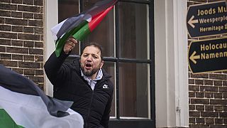 A man waves a Palestinian flag next to signs for the Holocaust Monument and the Jewish Museum as demonstrators protested against Israel's President Isaac Herzog.