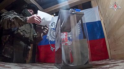 Um militar russo assiste à votação numa estação de voto improvisada durante a votação antecipada nas eleições presidenciais russas na região de Donetsk, controlada pela Rússia.