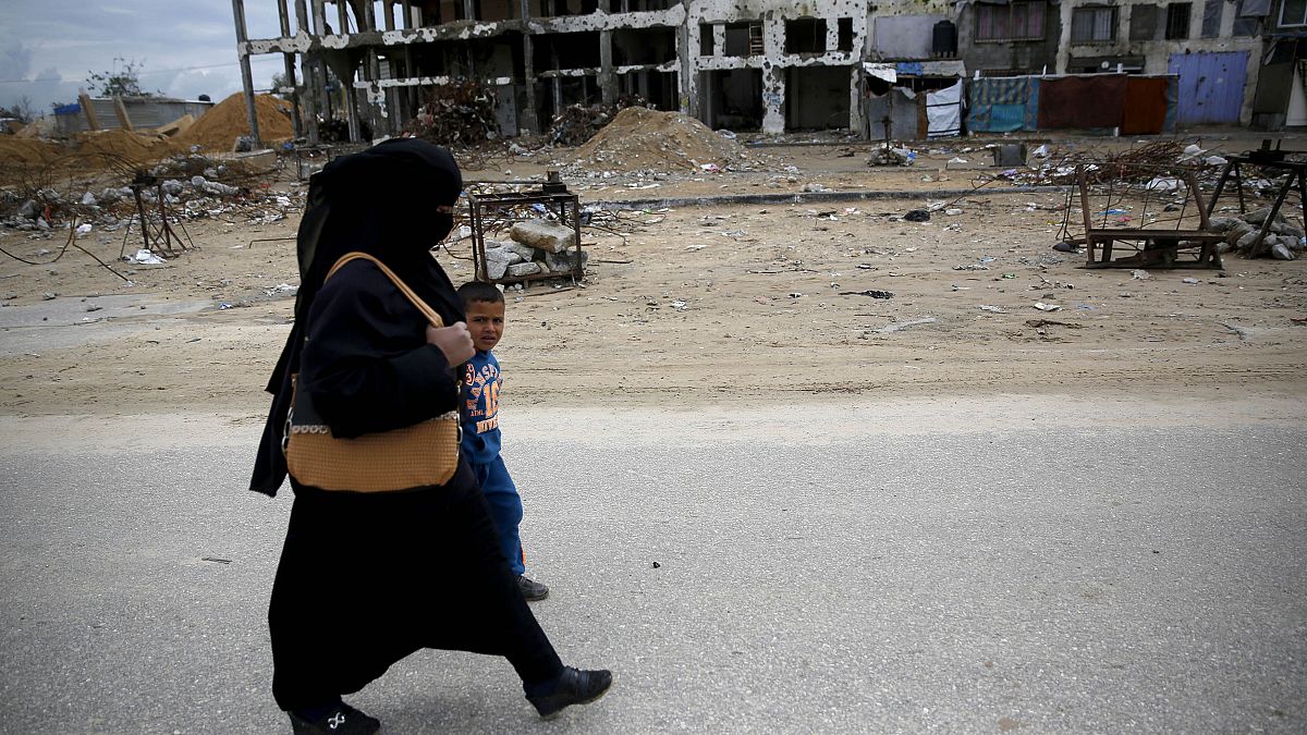 أم فلسطينية تسير مع طفلها عبر أجزاء من مبنى سكني مدمر