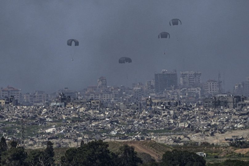 In a view from southern Israel, parachutes drop supplies into the northern Gaza Strip.