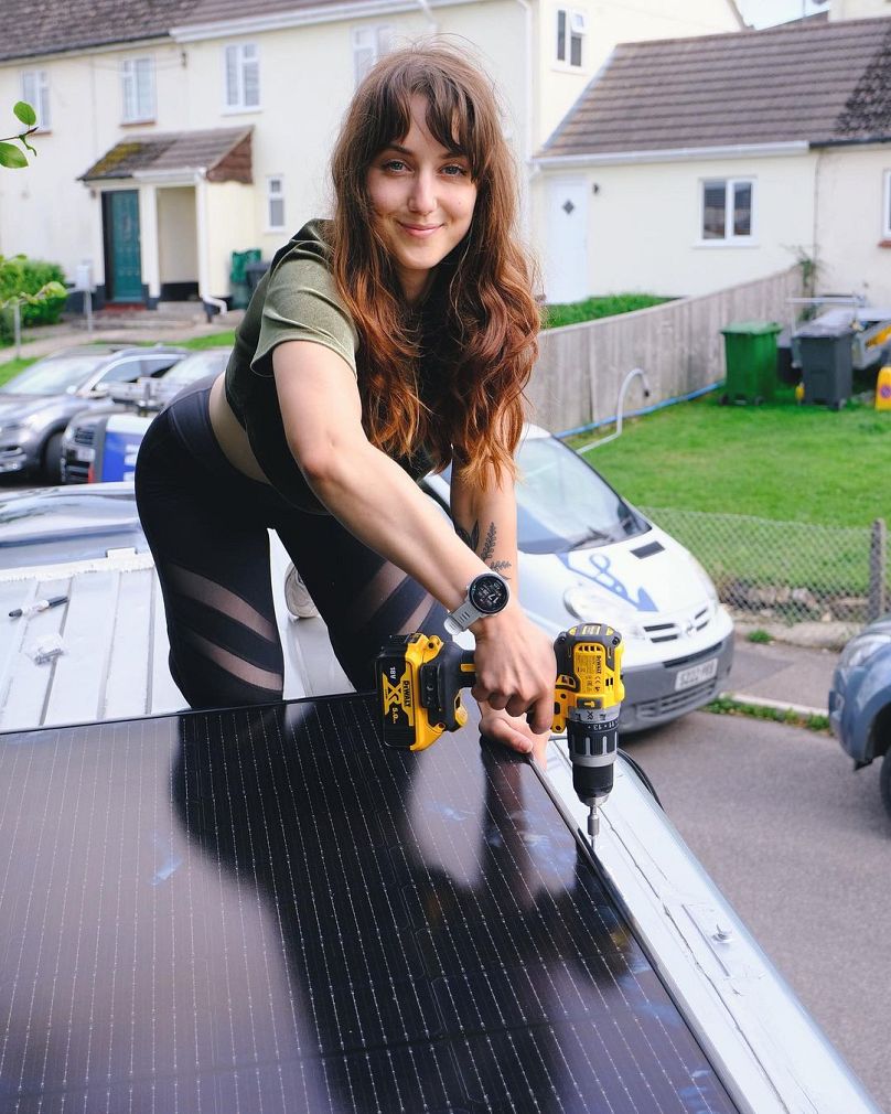 Jessica installing a 400W solar panel on the roof of the van. Despite driving, the couple have cut their carbon footprint by a third.