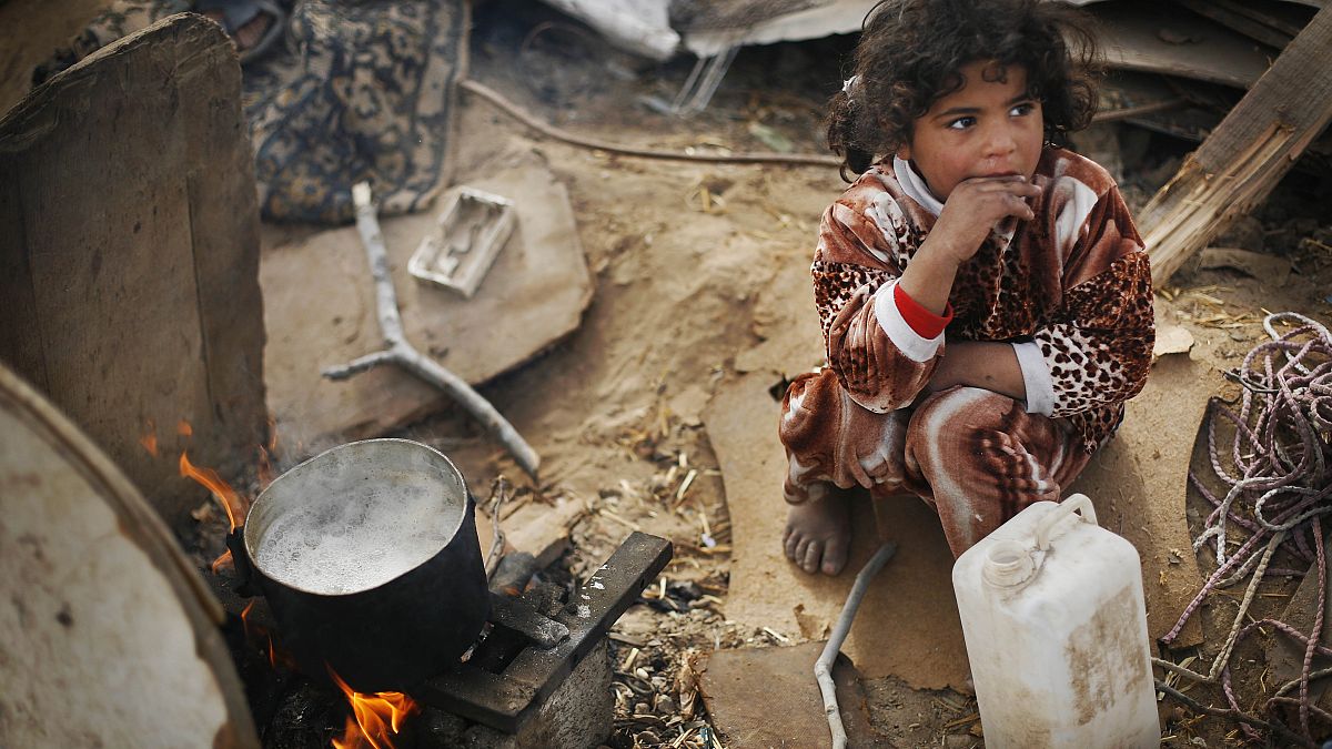 فتاة فلسطينية تجلس بجوار نار صغيرة بها ماء يغلي لصنع البطاطس