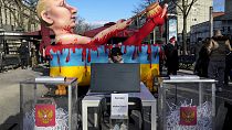 Макет урны для голосования с порванными бюллетенями и моделью президента Путина во время акции протеста возле избирательного участка у посольства России в Берлине