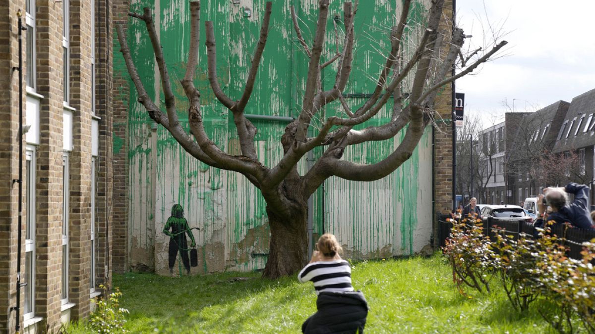 Des personnes regardent une nouvelle peinture de Banksy sur un mur à Londres, lundi 18 mars 2024. 