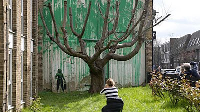 Des personnes regardent une nouvelle peinture de Banksy sur un mur à Londres, lundi 18 mars 2024. 