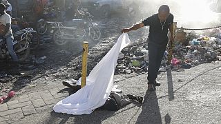 A person lifts a sheet to look at the identity of a body lying on the ground after an overnight shooting in the Petion Ville neighborhood of Port-au-Prince, Haiti, 18/3/24.