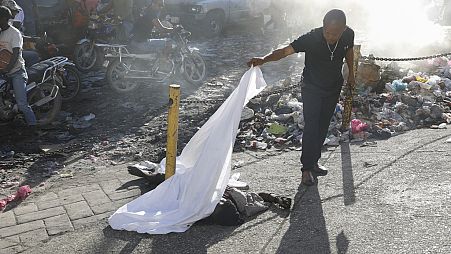 Una persona levanta una sábana para ver la identidad de un cuerpo después de un tiroteo en el barrio de Petion Ville de Puerto Príncipe, Haití, el 18 de marzo de 2024.