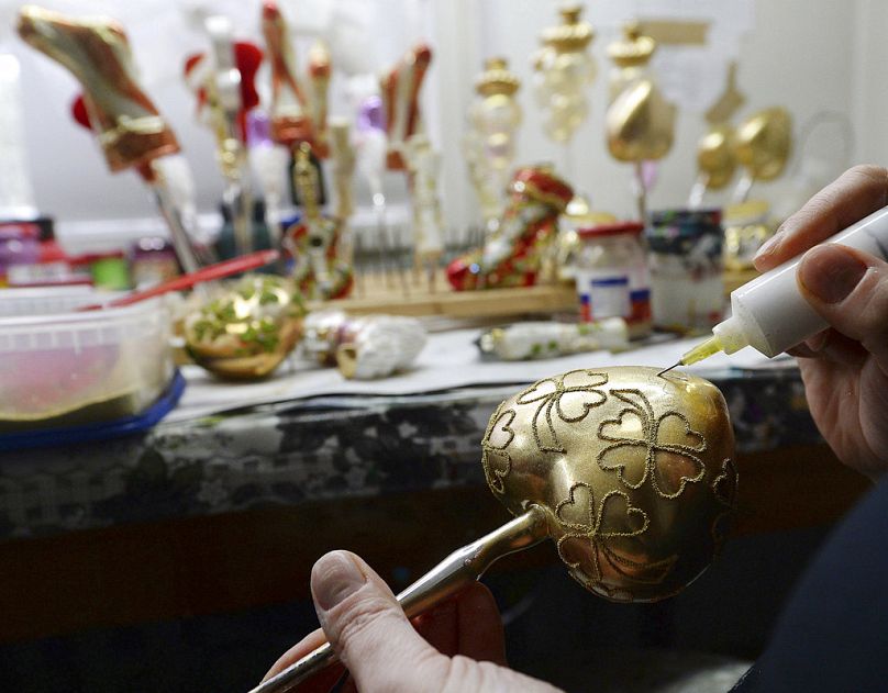 A painter decorates blown-glass Christmas tree ornaments with glitter at the Silverado manufacture in Jozefow, near Warsaw, November 2017