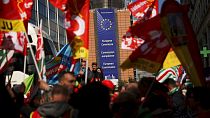 People listen to speeches near the European Commission headquarters, background, during a protest by European trade unions in Brussels, Friday, April 26, 2019.