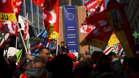 People listen to speeches near the European Commission headquarters, background, during a protest by European trade unions in Brussels, Friday, April 26, 2019.