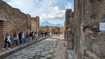 Turisták Pompeiiben, a háttérben a Vezúvval