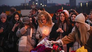 İnsanlar 23 Mart 2024 Cumartesi günü Moskova, Rusya'nın batı ucundaki Crocus Belediye Binası'nın yanında çiçek bırakıyor ve mum yakıyor. 