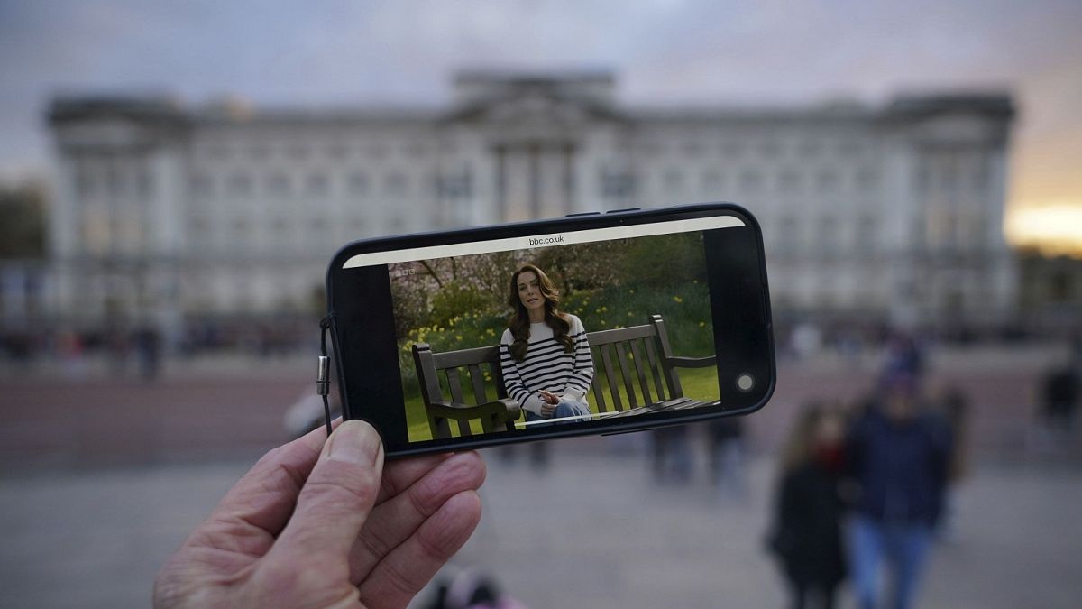 Uma pessoa assiste a um anúncio feito num smartphone no exterior do Palácio de Buckingham por Kate, a Princesa de Gales, sexta-feira, 22 de março de 2024.