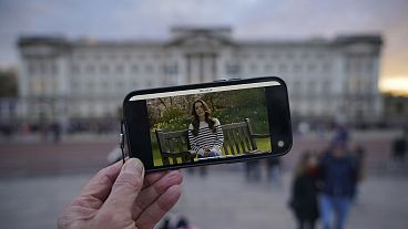 Uma pessoa assiste a um anúncio feito num smartphone no exterior do Palácio de Buckingham por Kate, a Princesa de Gales, sexta-feira, 22 de março de 2024.