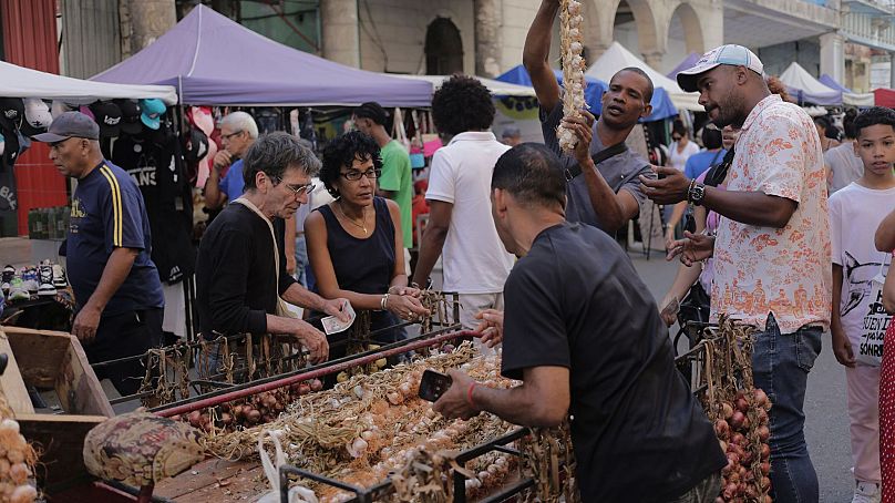 خریداران در یک بازار خیابانی در هاوانا، کوبا، دور یک گاری سیر جمع می‌شوند.