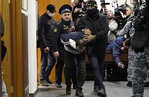Az egyik vádlottat rendőrök kísérik a moszkvai tárgyalóterembe.