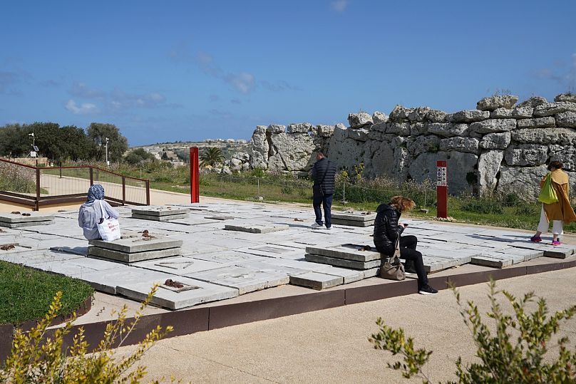 Visitors sitting and standing on Ibrahim Mahama’s installation “Garden of Scars,” with the Ġgantija Archaeological Park in the background.