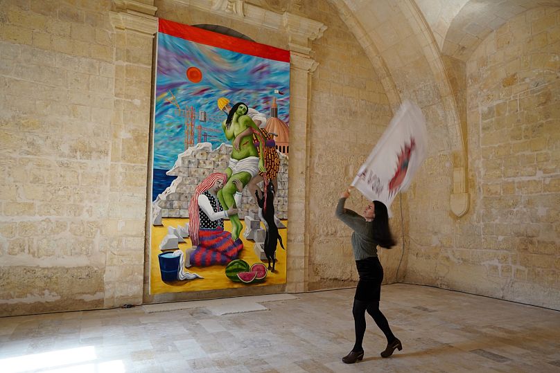 Italian artist Teresa Antignani waving a flag in front of her oil painting “Depozione (Deposition)”. She added watermelons as a symbol of Palestinian resistance, she said.