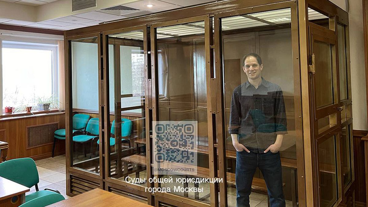 O repórter do Wall Street Journal, Evan Gershkovich, está de pé numa gaiola de vidro numa sala de audiências do Tribunal Municipal de Moscovo, em Moscovo, Rússia, terça-feira, 26 de março de 2024.