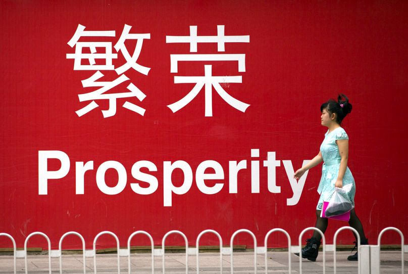 A woman walks past a sign reading "Prosperity" in Chinese and English in Beijing, July 2015