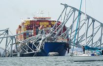 A sailboat passes by a cargo ship is stuck under the part of the structure of the Francis Scott Key Bridge after the ship hit the bridge Tuesday March 26, 2024, in Baltimore.