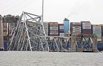 Az összedőlt híd, a háttérben a hajón tornyosuló konténerekkel