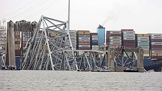 Az összedőlt híd, a háttérben a hajón tornyosuló konténerekkel