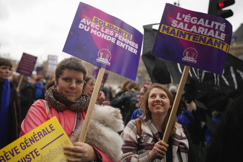 Women demonstrate with posters reading "Equal pay now", right, and "Solidarity with women around the world" as part of the International Women's Day in Paris, March 2023