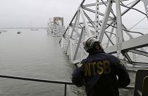 Az amerikai Országos Közlekedésbiztonsági Hivatal szakértője vizsgálódik a baltimore-i híd acélszerkezetének roncsai alá szorult hajón 2024.03.27-én. 