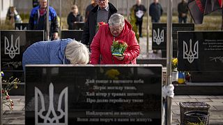 A crying relative waits to place flowers on the grave of a fallen Ukrainian serviceman during a commemoration for the victims of the Russian occupation at a cemetery in Bucha,