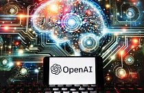 The OpenAI logo is seen displayed on a cell phone with an image on a computer screen generated by ChatGPT's Dall-E text-to-image model, Friday, Dec. 8, 2023, in Boston. 