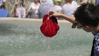 طفل يغطس قبعته في حوض نافورة في يوم حار في ساحة القديس بطرس في الفاتيكان. 2023/07/16