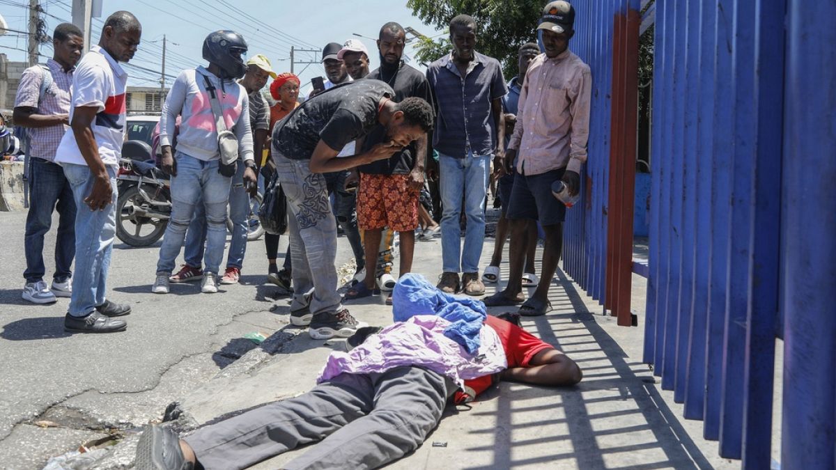 People observe the body of a man lying on the street of the Delmas 30 neighborhood in Port-au-Prince, Haiti, Monday, April 1, 2024