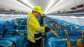 A WISAG employee secures plastic boxes full of mail covered with fabric sleeves to the passenger seats of an Airbus at Berlin Brandenburg Airport, in Schönefeld, Germany.