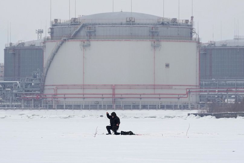 Un uomo pesca sul ghiaccio del Golfo di Finlandia sullo sfondo dei serbatoi di petrolio di San Pietroburgo