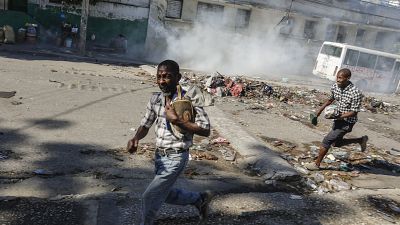 Homens correm para se abrigar enquanto a polícia de choque lança gás lacrimogéneo numa tentativa de dispersar as pessoas perto do Palácio Nacional, em Port-au-Prince, Haiti,.