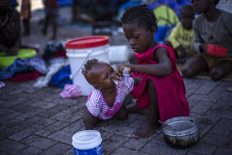 A girl helps a baby to drink water at a square transformed into a refuge for families forced to leave their homes due to clashes between gangs, in Port-au-Prince, October 2022