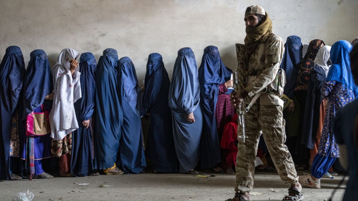 یک جنگجوی طالبان در حالی که زنان منتظر دریافت جیره غذایی توزیع شده توسط یک گروه کمک‌های بشردوستانه در کابل هستند، نگهبانی می‌کند