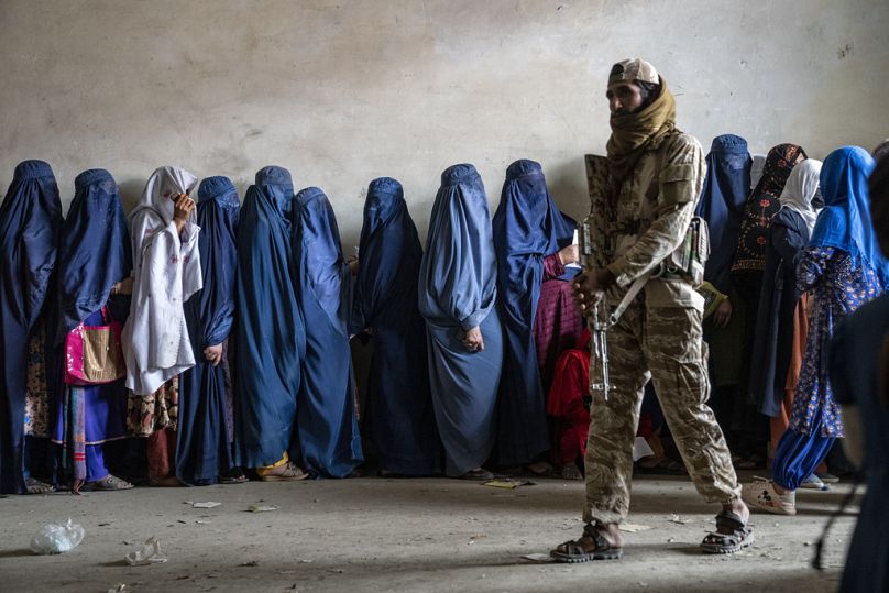 A Taliban fighter stands guard as women wait to receive food rations distributed by a humanitarian aid group, in Kabul, May 2023
