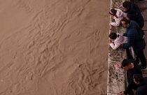 Un grupo de gente observa el río Guadalquivir tras las recientes lluvias bajo el puente romano en Córdoba, España