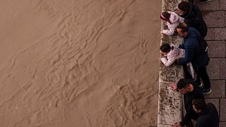 Un grupo de gente observa el río Guadalquivir tras las recientes lluvias bajo el puente romano en Córdoba, España