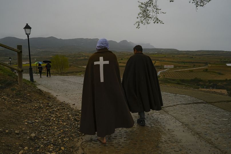 A hooded penitent, left, and his assistant walk as the rain falls at the end of the procession known as "Los Picaos" on Holy Friday.